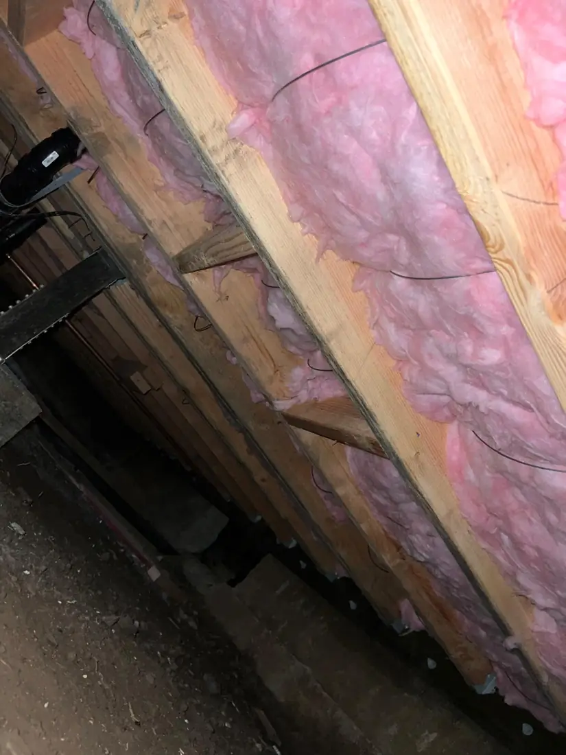 Pink fiberglass batts between floor joists viewed from inside a crawl space