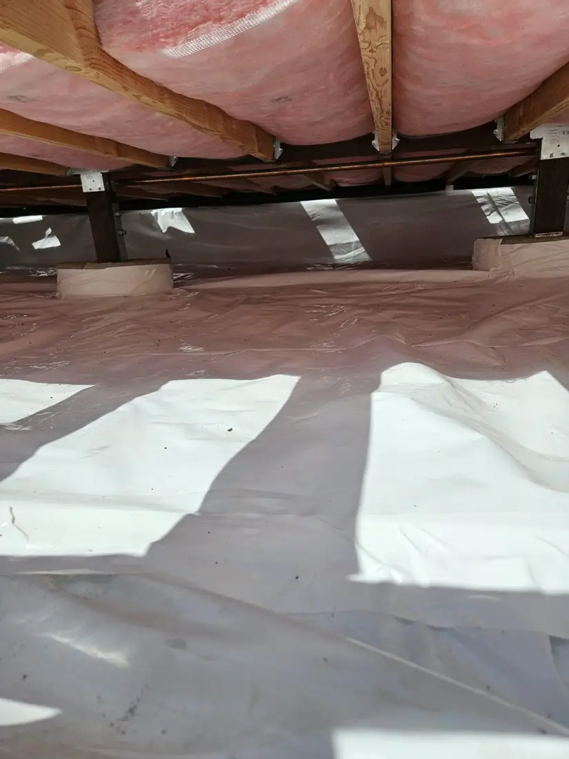 Wide view of a crawl space with a white ground vapor barrier and insulated floor above