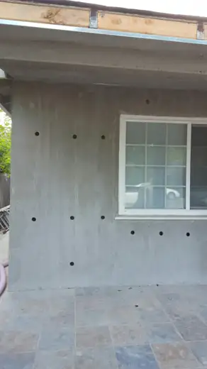 Stucco exterior wall with drill and fill holes being filled with insulation