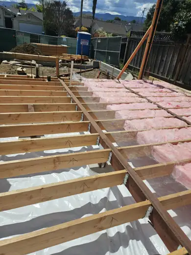 Floor joists being insulated over a vapor barrier