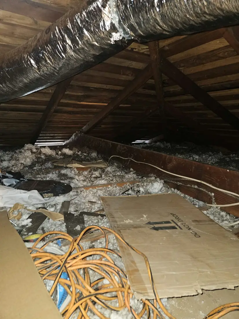 Attic with old insulation, debris and cardboard before cleanup